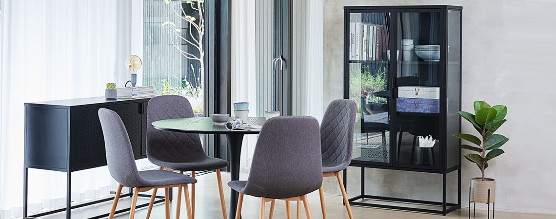 Vitrine en verre dans une salle à manger, avec une table ronde et chaises grises.