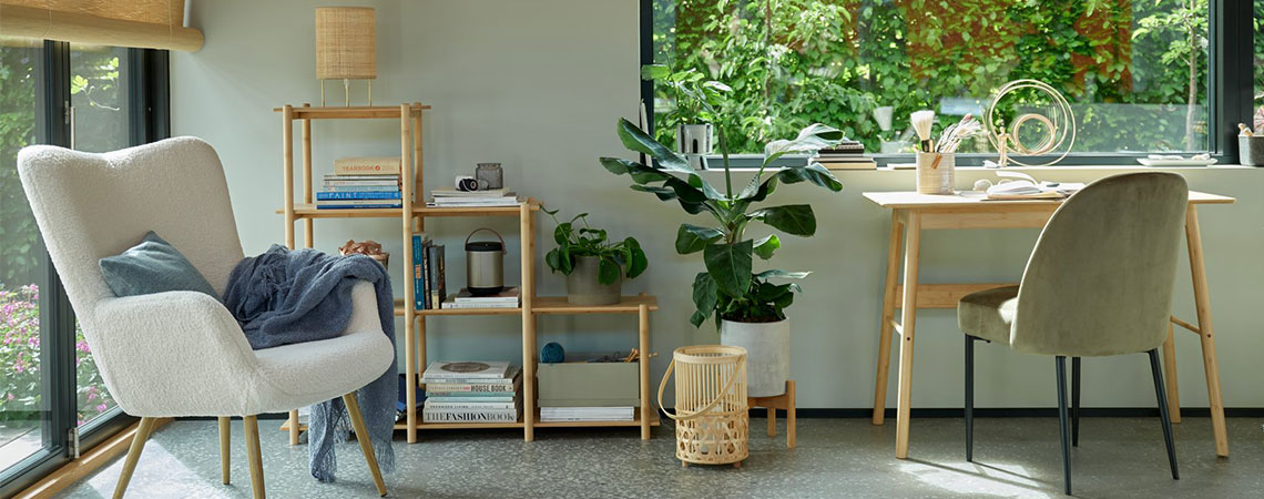 Fauteuil gris près d'une fenêtre et un diviseur d’espace en bambou à l'arrière-plan. Lanterne en bambou au sol à côté d'un bureau en bambou et d'une chaise de salle à manger vert olive