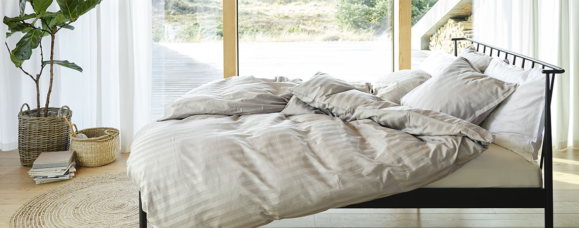 Chambre à coucher avec un lit en métal, couette et oreillers, et une parure de lit rayée en gris et blanc