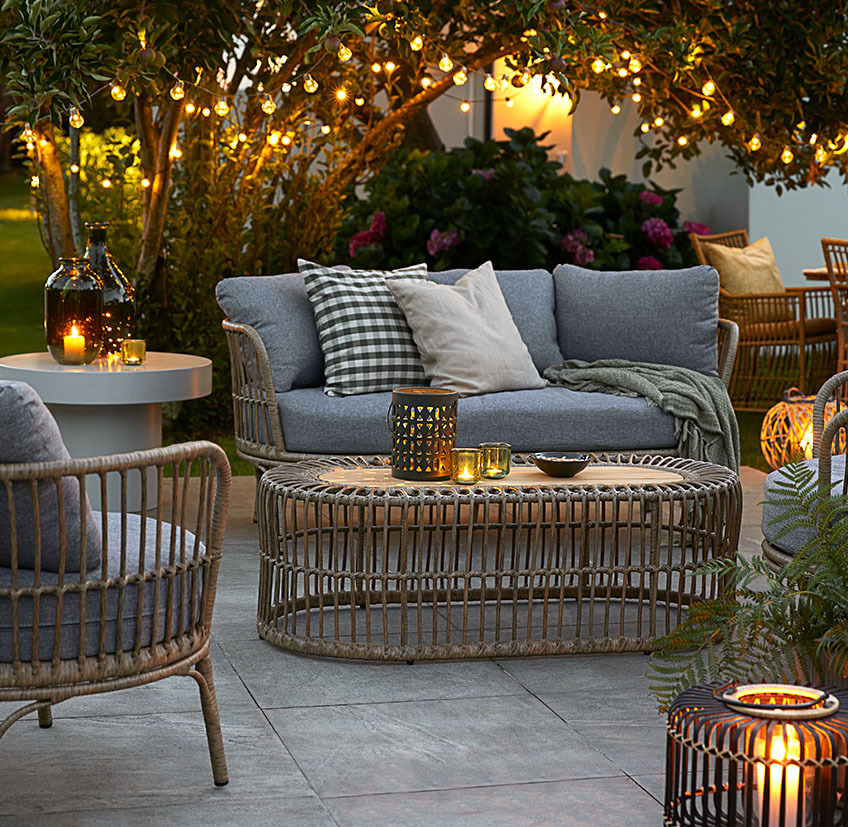 Mobilier de jardin sur un patio avec des guirlandes lumineuses, lampes à piles et lanternes avec bougies et bougies chauffe-plat