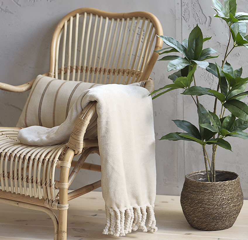 Jeté beige sur chaise longue en rotin et plante artificielle en cache-pot