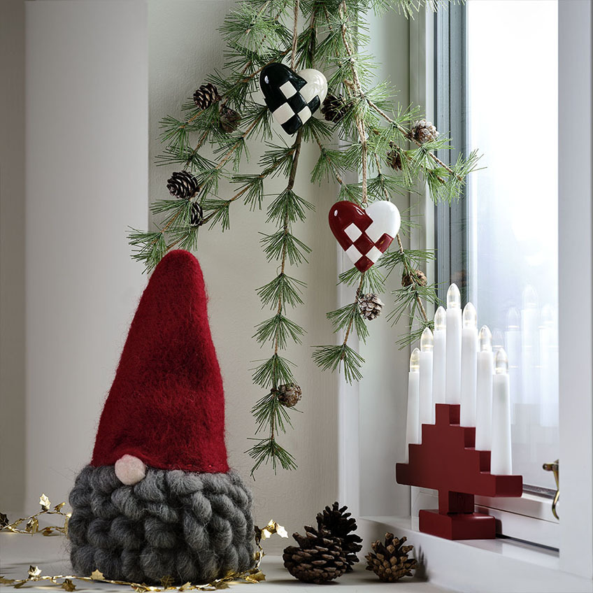 Lutin de Noël MUGGLESTEN, cœur de Noël PYSSEL, et pont de bougie HILDEGUN. Lutin de Noël avec un bonnet rouge et une barbe grise, cœurs de Noël et pont de bougie rouge.