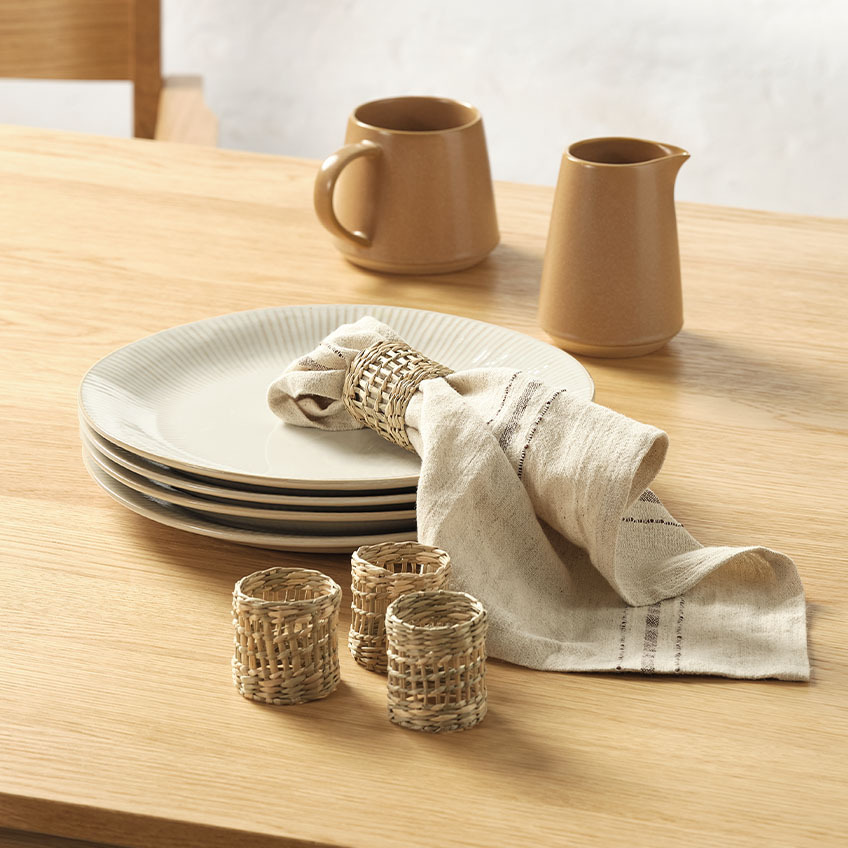 Assiettes blanches cannelées, pots à lait, serviette tissu et ronds de serviette sur table à manger