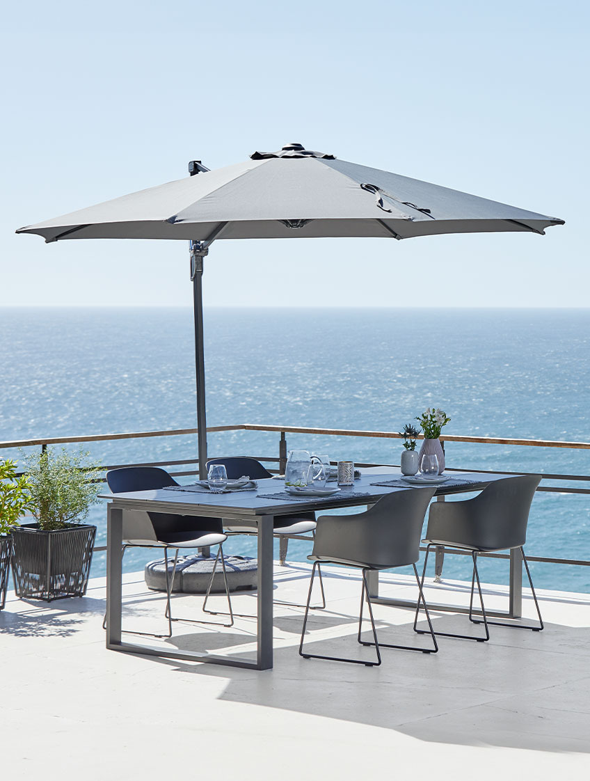 Grand parasol déporté et table et chaises de jardin sur une terrasse avec vue mer