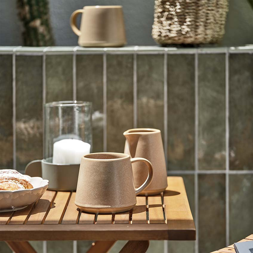 Tasse à café et pot à lait sur une petite table en bois au soleil