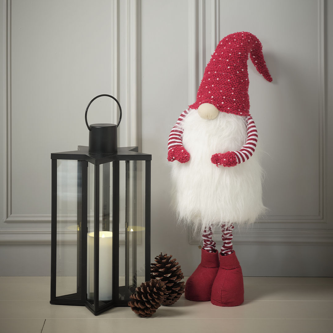 Grand lutin de Noël avec un bonnet rouge et une longue barbe à côté d’une lanterne noire en forme d’étoile