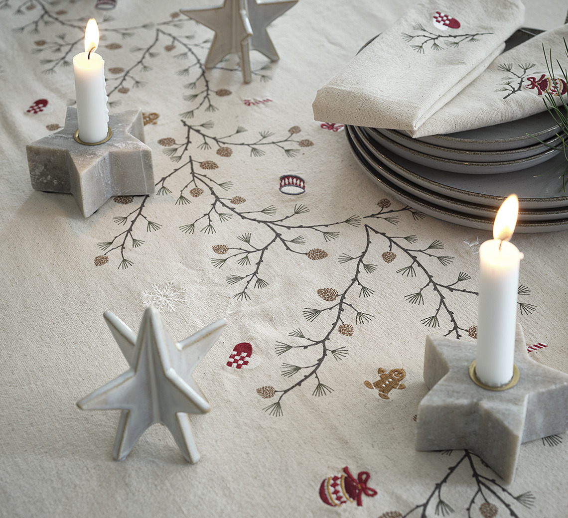 Table à manger avec nappe de Noël, chandeliers en forme d’étoile, assiettes et décorations