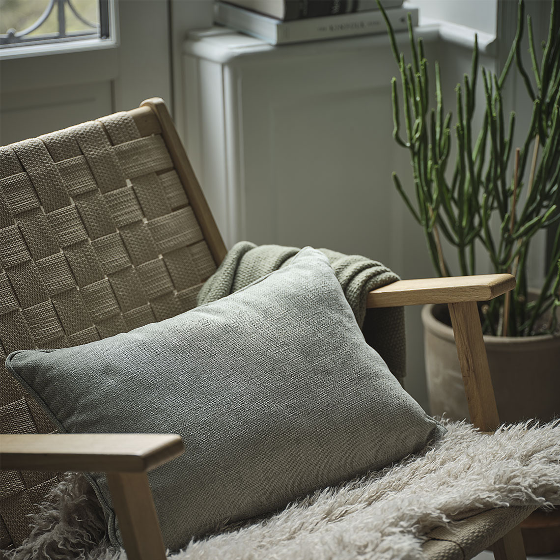 Coussin vert sur une chaise avec un plaid vert et une fausse fourrure d’agneau beige