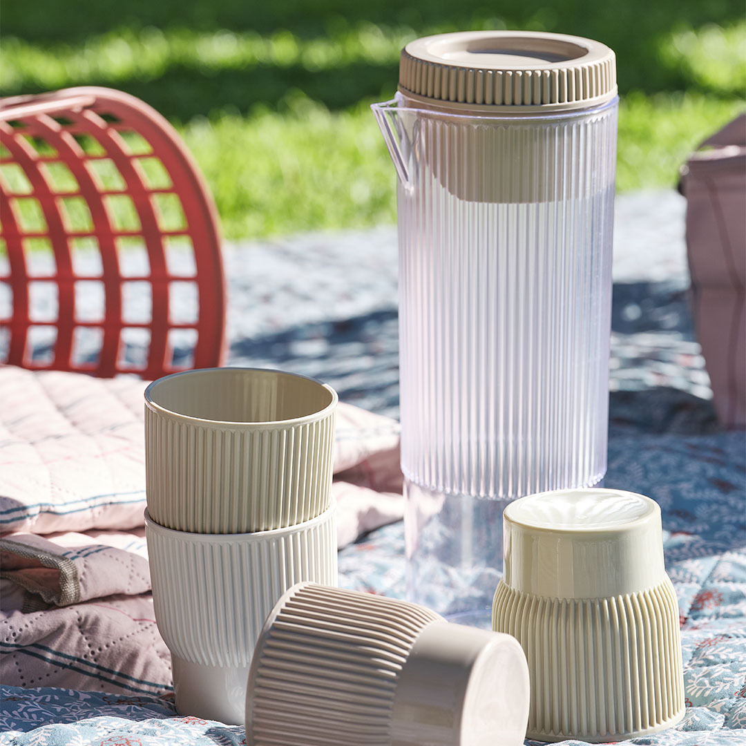 Essentiels de pique-nique, y compris une carafe avec quatre tasses assorties sur une couverture de pique-nique