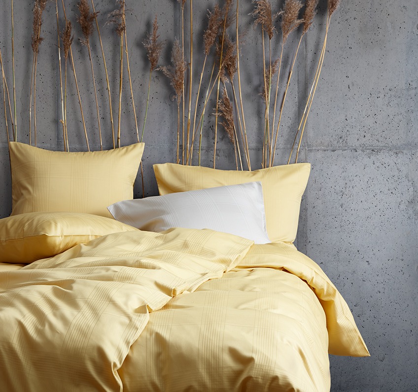 CILJE bed linen in yellow Yellow bed linen out of 51% recycled polyester and 49% cotton sateen in a bedroom with concrete walls