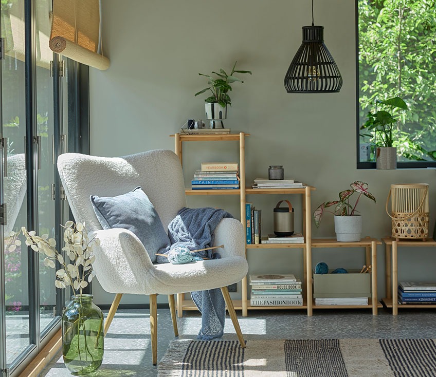 Fauteuil gris près d'une fenêtre avec un vase au sol vert et un séparateur de pièce en bambou à l'arrière-plan