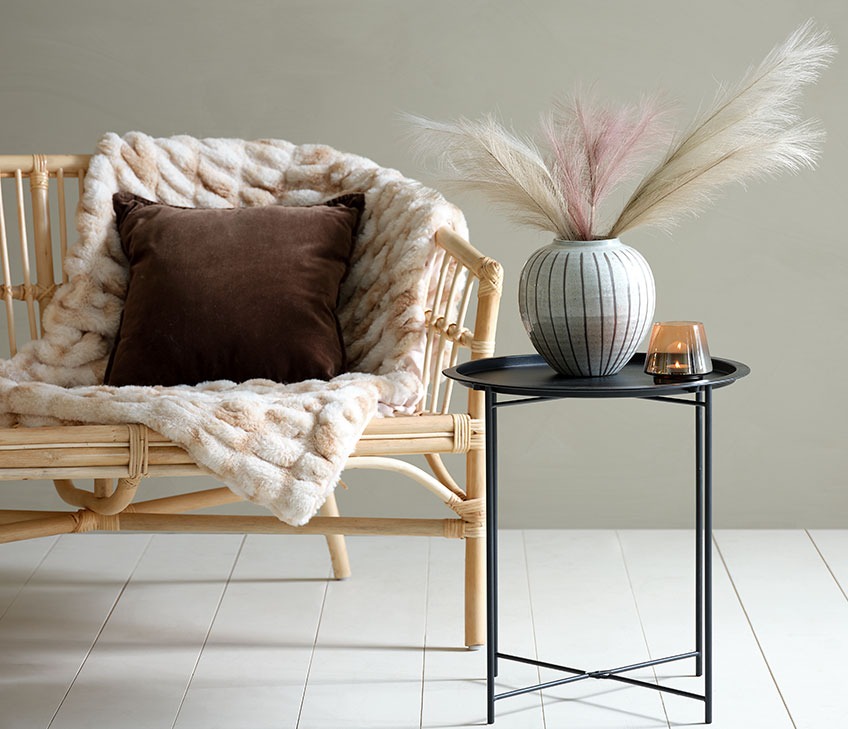 Canapé avec plaid en fausse fourrure et coussin brun. Table basse noire, avec vase et photophore