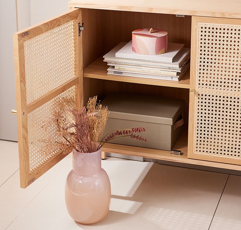 Vase soufflé bouche avec un bouquet de fleurs artificielles, devant un buffet avec une porte ouverte et une boîte de rangement ronde.