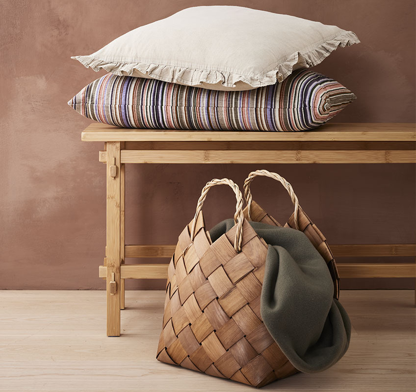 Coussins BANKSIA et GULDBLOMME, panier ABEL, plaid DAGLILJE Coussins décoratifs sur un banc en bois avec un panier et un plaid