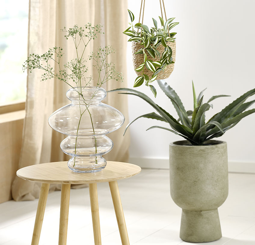 Vase en verre sur une table d’appoint, pot de fleurs suspendu et pot de fleurs avec une plante artificielle
