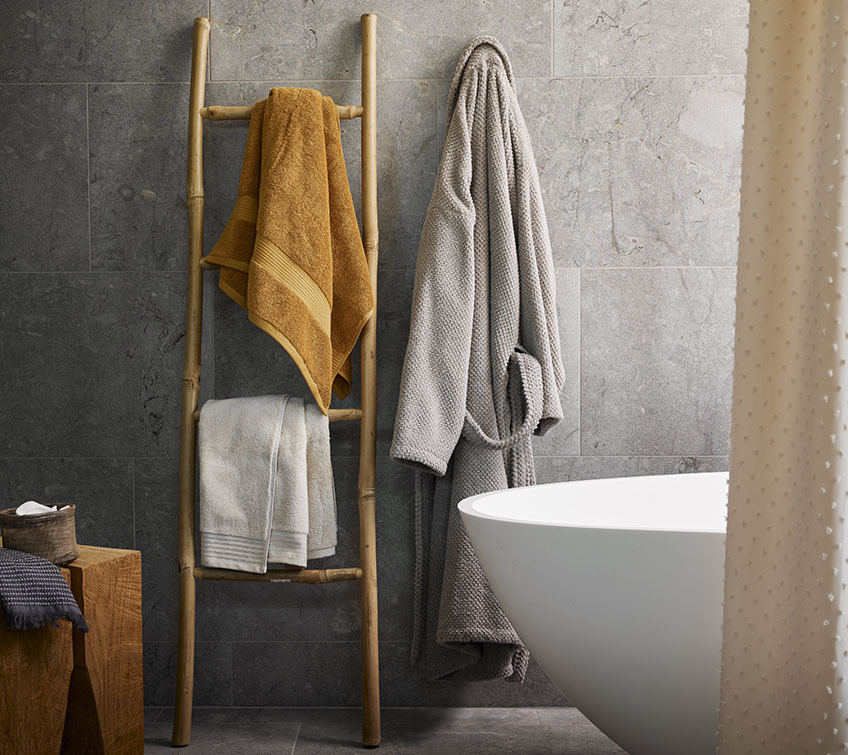 Serviettes KARLSTAD, et SORUNDA, peignoir BULLMARK Echelle décorative avec des serviettes blanches et jaunes et un peignoir gris dans une salle de bain